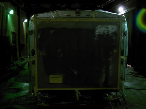 1900 Ford C-350 (Centurion Conversions) - A large trailer is covered in protective plastic sheeting inside a dimly lit building.