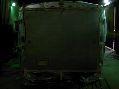 1900 Ford C-350 (Centurion Conversions) - The rear of a large box truck or trailer, covered in protective plastic wrap, is shown in a dimly lit indoor space.