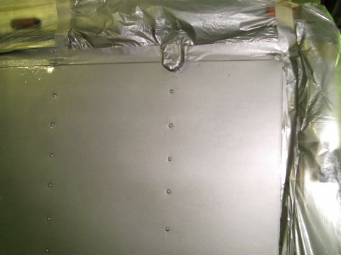 1900 Ford C-350 (Centurion Conversions) - A close-up view of a gray metal panel with visible rivets, partially covered by protective plastic sheeting.