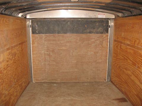 1900 Ford C-350 (Centurion Conversions) - The interior of a cargo trailer is shown, wood paneling on the walls and floor, with metal trim around the doorway.
