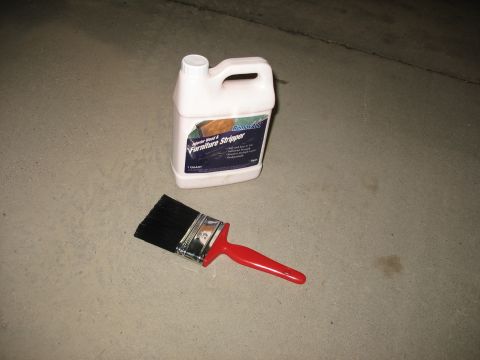 1900 Ford C-350 (Centurion Conversions) - A bottle of furniture stripper and a paintbrush lie on a concrete surface, suggesting a DIY or restoration project.