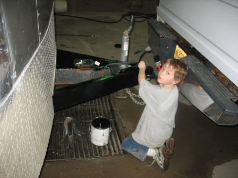 1900 Ford C-350 (Centurion Conversions) - A young boy paints a trailer hitch while near the bumper of a white vehicle.