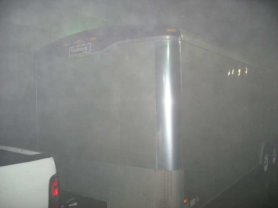Silver enclosed trailer with a Haulmark logo, partially obscured by fog. A white truck is visible on the left