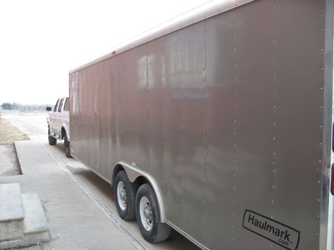 1900 Ford C-350 (Centurion Conversions) - A pickup truck is seen from the side, towing a large gray Haulmark trailer on a paved surface.