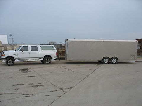 1900 Ford C-350 (Centurion Conversions) - White Ford Bronco SUV towing a large silver enclosed trailer on a paved lot.