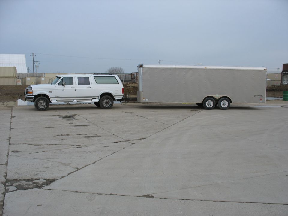 White Ford SUV towing a silver enclosed trailer on a concrete lot