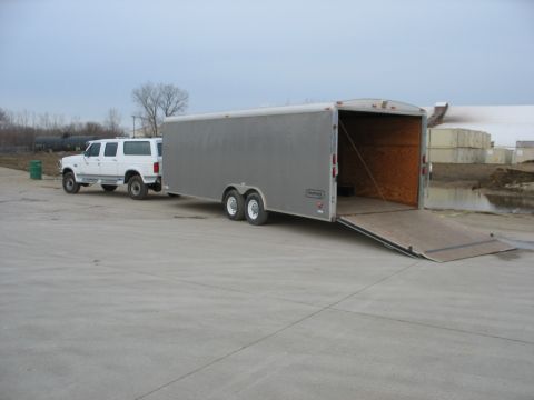 1900 Ford C-350 (Centurion Conversions) - A white SUV is parked next to a large, open enclosed trailer on a cloudy day.