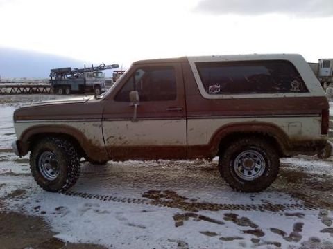 1985 Ford Bronco - Side view of a muddy 1985 Ford Bronco in a snowy, outdoor setting.