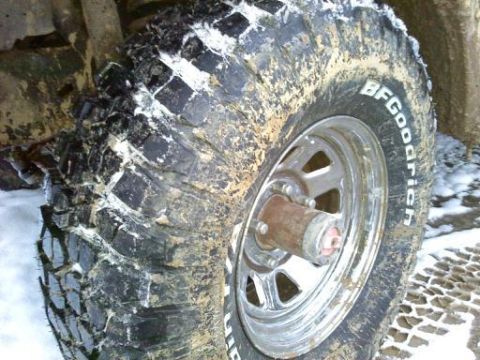 1985 Ford Bronco - Close-up of a dirty off-road tire with visible tread and sidewall markings, set against a snowy background.