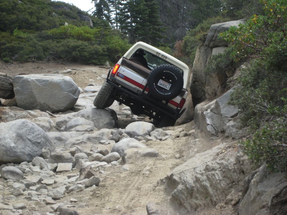 White and brown Ford Bronco navigating a rocky trail, rear view