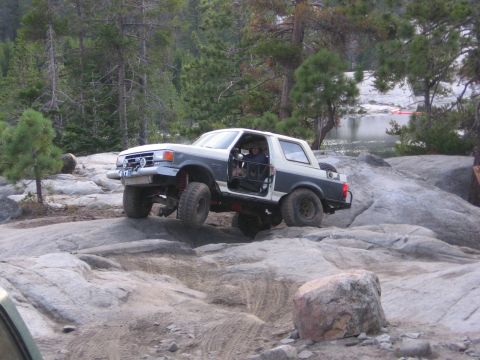 1991 Ford Bronco - This modified Ford Bronco is shown off-roading over large rocks in a wooded area.
