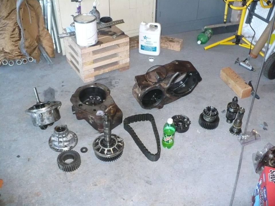 Disassembled chain-drive transfer case parts laid out on a garage floor with case halves, chain and gears
