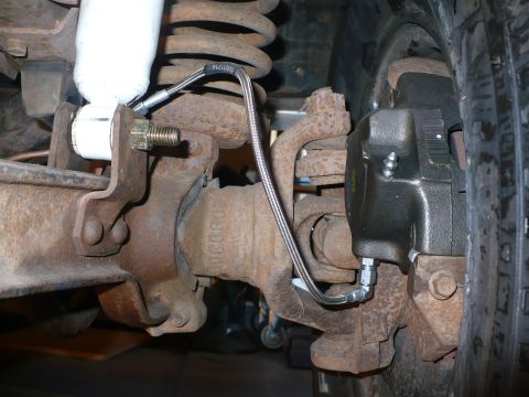 1979 Ford Bronco - Underside close-up of a solid front axle with a new braided stainless steel brake line routed from the axle housing bracket down to the dis…