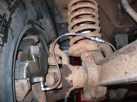 1979 Ford Bronco - Front suspension detail shot showing a braided stainless Earl's brake line routed from the frame down to a cast disc brake caliper, alongsi…