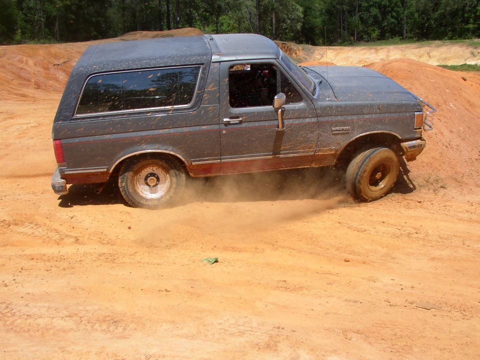Dark Ford Bronco spinning tires and throwing dirt on an orange clay off-road bank