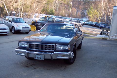 2001 Ford Crown Victoria - A dark sedan is parked in a lot with other vehicles and trees in the background.