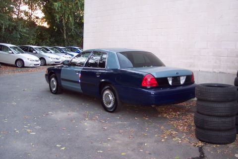 2001 Ford Crown Victoria - A two-tone sedan is parked in front of a building with other vehicles in the background.