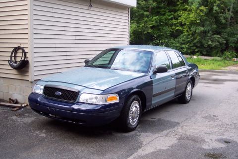 2001 Ford Crown Victoria - A two-tone blue 2001 Ford Crown Victoria is parked on wet asphalt near a building.