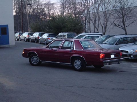 2001 Ford Crown Victoria - This maroon sedan, likely from the 1980s, is parked in a lot alongside several other vehicles.