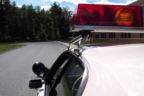 2001 Ford Crown Victoria - A close-up view of a police car's light bar and side mirror, set against a backdrop of trees and a building.