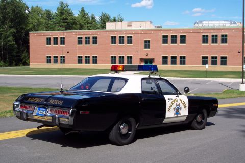 2001 Ford Crown Victoria - A vintage police car with a light bar is parked in front of a brick building.