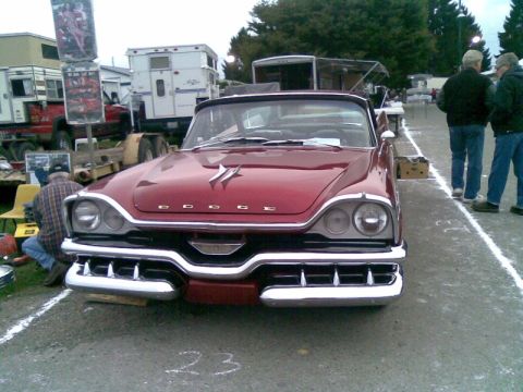 1969 Lincoln Continental - A red 1957 Dodge Custom Royal convertible is displayed at an outdoor event, with people and trailers in the background.