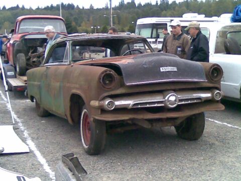 1969 Lincoln Continental - This heavily rusted sedan, likely a 1955 model, is seen from the front 3/4 angle with a custom hood and red-rimmed wheels.