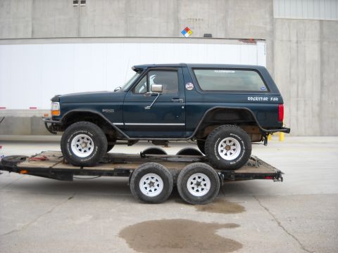 1900 Ford C-350 (Centurion Conversions) - Dark blue Ford Bronco with "ROCKSTAR FAB" decal on the rear quarter panel is loaded onto a trailer.