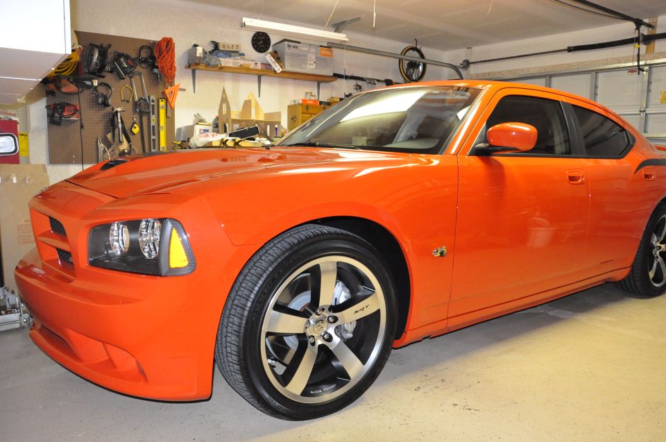 Orange Dodge Charger parked in a garage. It has custom wheels with SRT branding