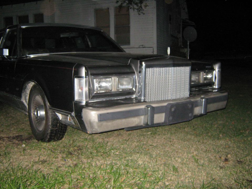 Front of a dark-colored Lincoln Town Car parked on grass at night