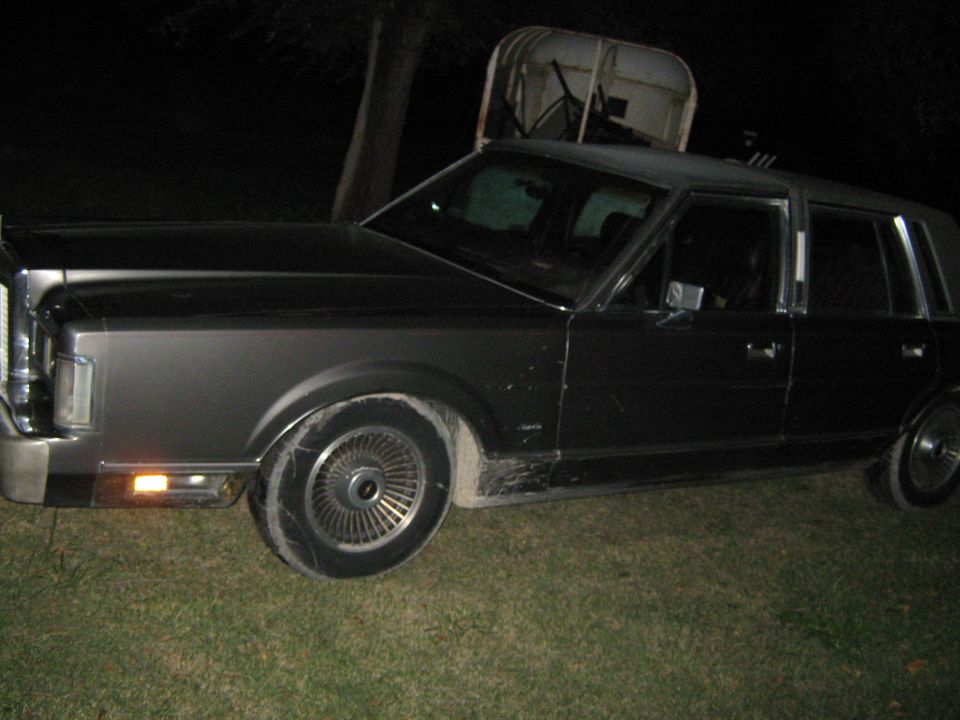 Dark sedan parked on grass at night. Has a chrome grille and distinct wheel covers