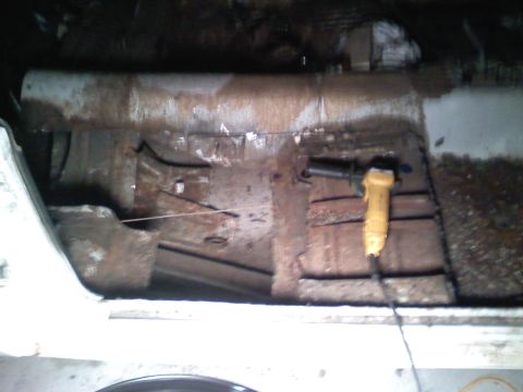 1969 Ford Mustang - A yellow angle grinder rests on the rusty floor of a car interior.