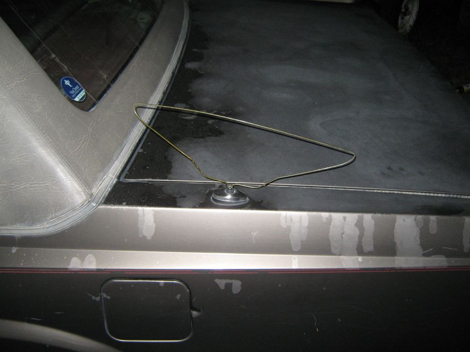 Car trunk lid with a wire coat hanger resting on it. A fuel door is visible on the lower left