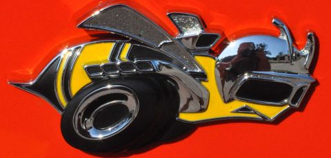 1973 Ford Ranchero - A close-up of a chrome and yellow bee emblem with black accents on an orange background, possibly car-related, surface.