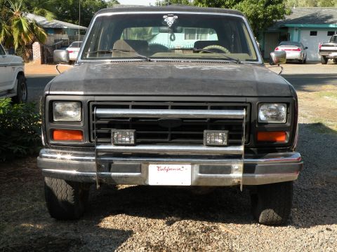 1986 Ford Bronco - Front view of a dark-colored Ford Bronco, likely from the early 1980s, with a custom grille and auxiliary lights.