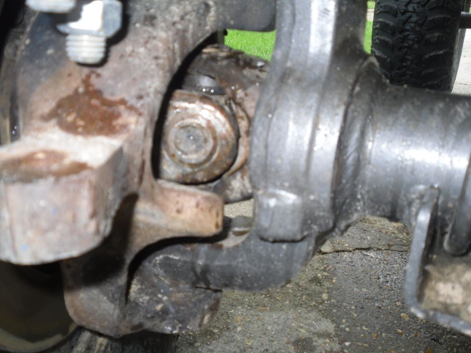 Close-up of a rusty, greasy vehicle suspension part with a tire visible in the background