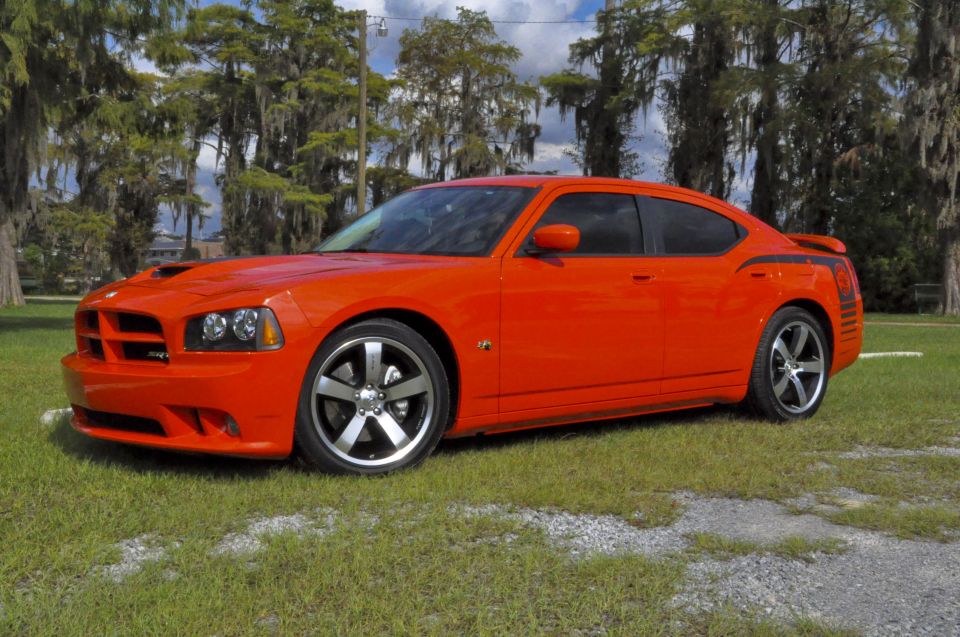Orange Dodge Charger SRT8 Super Bee, front 3/4 view on grass under mossy oaks