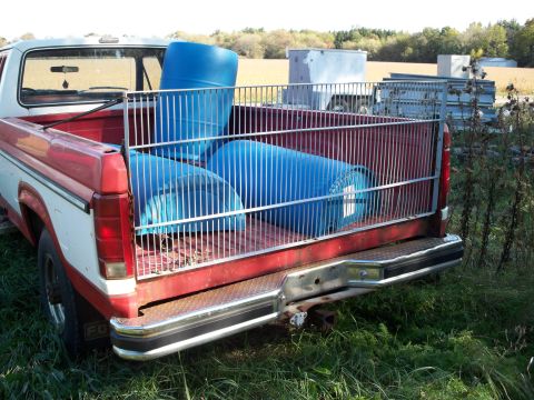 1988 Ford F-150 - The rear of a red and white Ford F-150 pickup truck is shown, loaded with blue barrels.