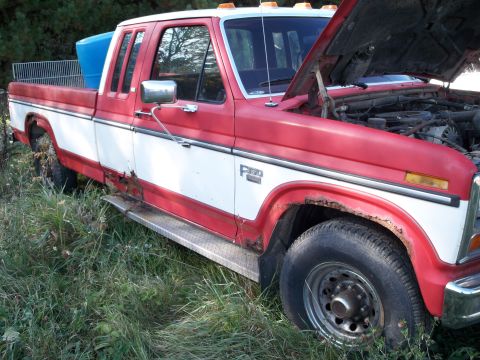 1988 Ford F-150 - This red and white Ford F-150 pickup truck has rust and its hood is open.