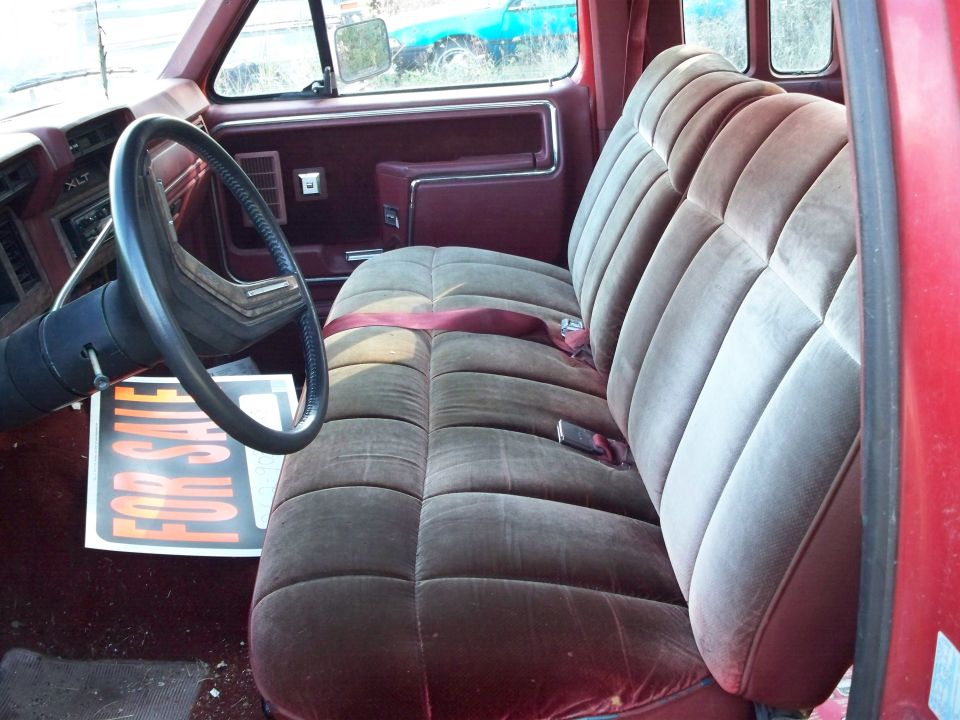 Red truck interior with velour bench seat, steering wheel, and "FOR SALE" sign