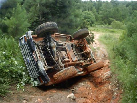 1985 Ford Bronco - This vehicle has rolled over on a wooded dirt road, showing its undercarriage and wheels.