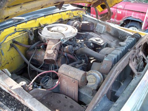 1988 Ford F-150 - The engine bay of a yellow truck shows significant rust and wear, with another vehicle in the background.