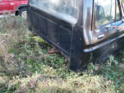 1988 Ford F-150 - A black pickup truck cab and bed sits in overgrown grass next to a red truck.