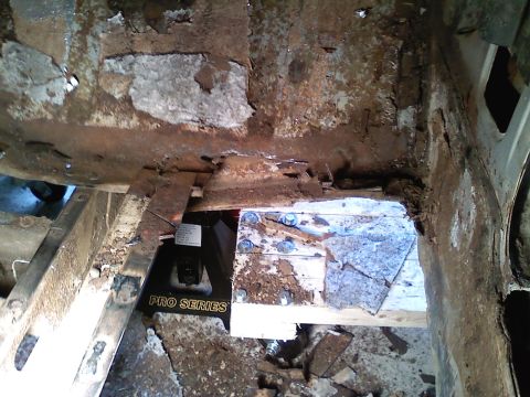 1969 Ford Mustang - Extensive rust damage is visible on the car's frame, supported by a jack and wooden bracing.