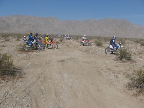 1996 Ford C-350 (Centurion Conversions) - A group of dirt bikes and riders are gathered on a dry, dusty track in a desert landscape.