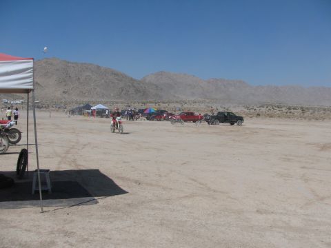 1996 Ford C-350 (Centurion Conversions) - A dirt bike race is underway in a desert landscape with mountains in the distance and several vehicles and tents set up.