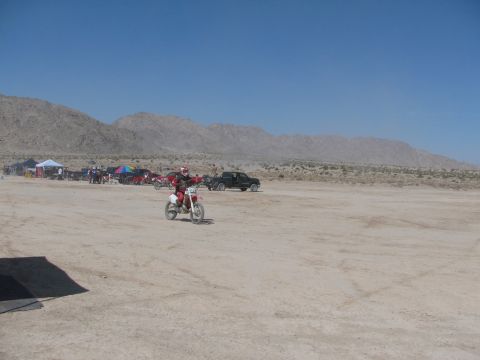 1996 Ford C-350 (Centurion Conversions) - A dirt bike rider is seen in a wide, sandy area with mountains in the distance and several vehicles parked.
