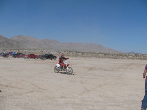 1996 Ford C-350 (Centurion Conversions) - Dirt bike rider in desert with parked trucks and mountains in background.