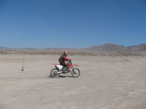 1996 Ford C-350 (Centurion Conversions) - A rider on a dirt bike navigates a dusty, arid terrain under a clear blue sky.
