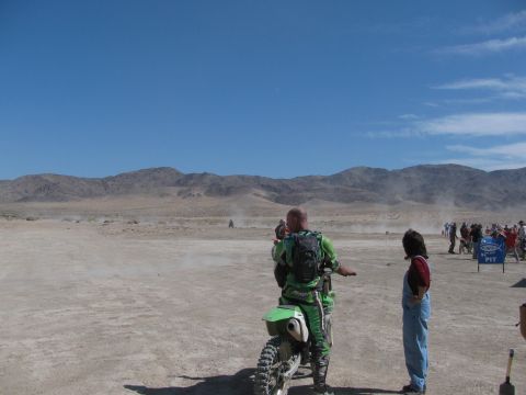 1996 Ford C-350 (Centurion Conversions) - A dirt bike race is underway in a dusty desert environment, with riders and spectators gathered in the pit area.